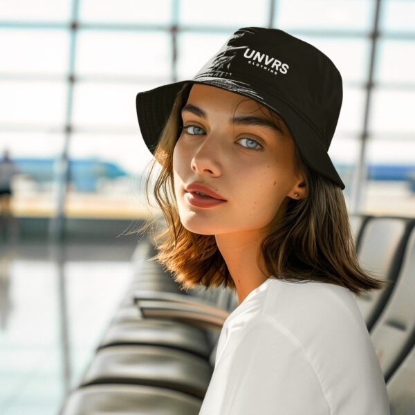 Female model wearing a UNVRS bucket hat featuring the brand’s logo prominently on the front. The hat’s classic silhouette and minimalist design offer a stylish and practical accessory, perfect for completing any streetwear look. Ideal for sunny days and festivals, it captures the playful yet edgy vibe of Ibiza’s fashion scene