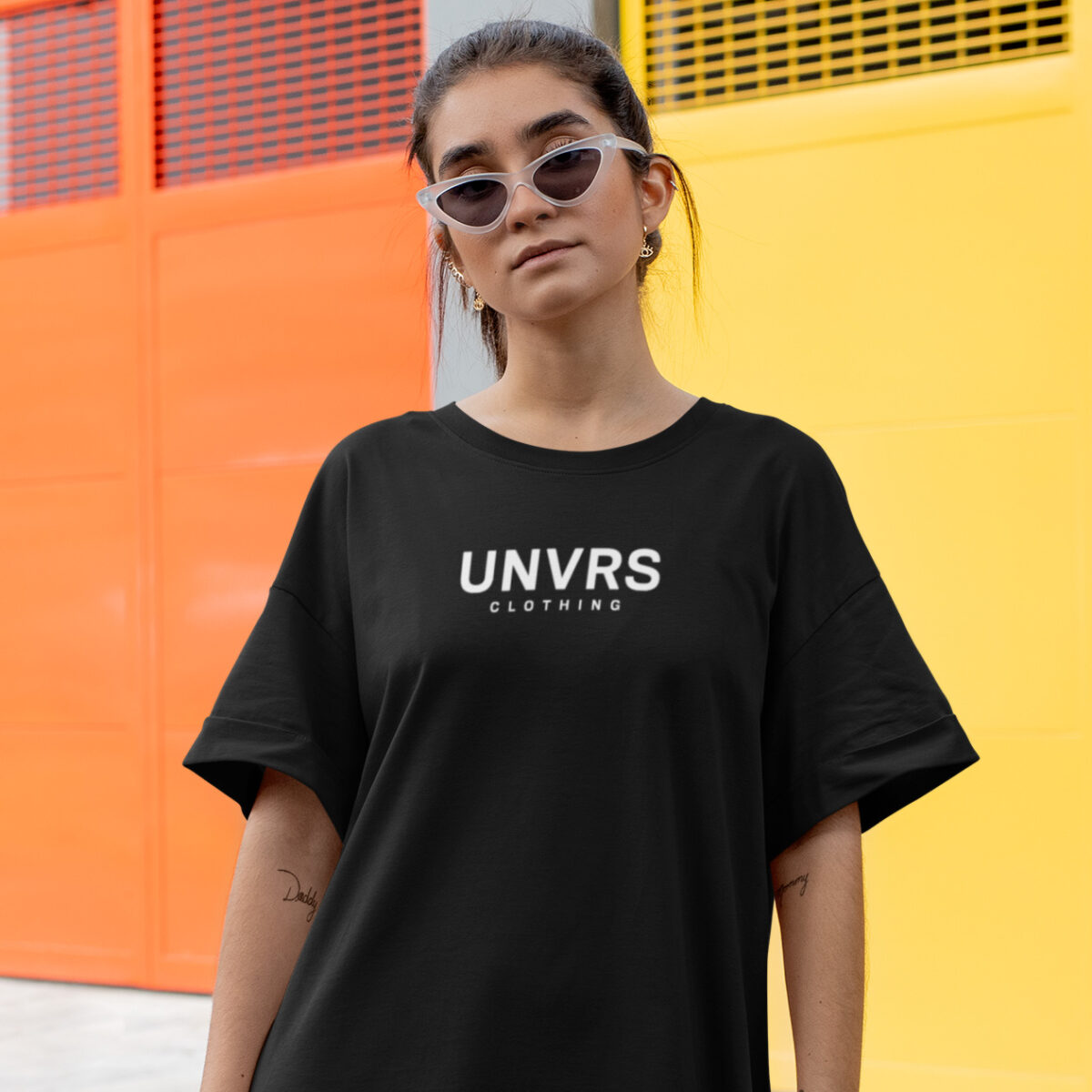 Female model wearing a loose-fit UNVRS t-shirt, styled for a relaxed, casual look. The oversized silhouette offers both comfort and effortless streetwear appeal, making it an ideal choice for layering or pairing with leggings and jeans. Perfect for embracing Ibiza’s laid-back yet edgy fashion aesthetic.